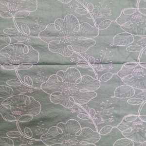 Large stylized two tone floral motifs are outlined with thick, rope-like embroidery, giving it a 3D effect on a sage green colour linen look fabric base.