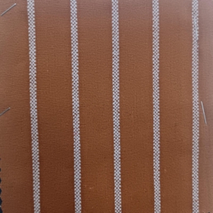 A rust and white stripe on a surface with natural slubs and irregular threads, very characteristic of linen.