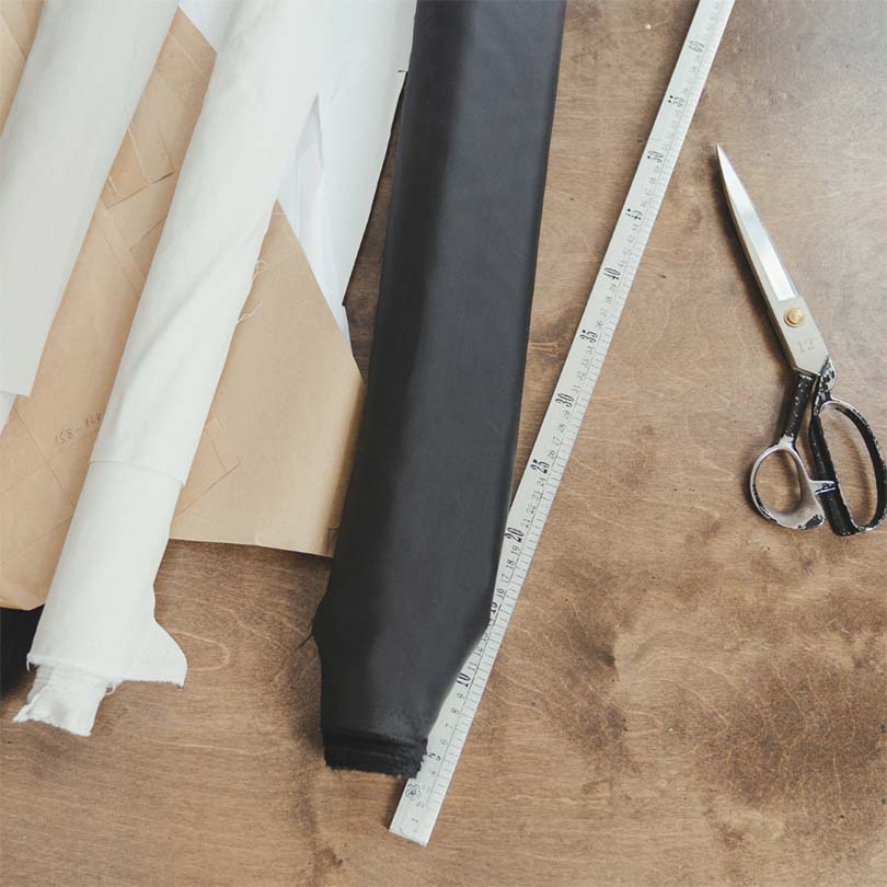 Metal ruler, scissor, patternmaking paper and 2 rolls of fabric on a table.