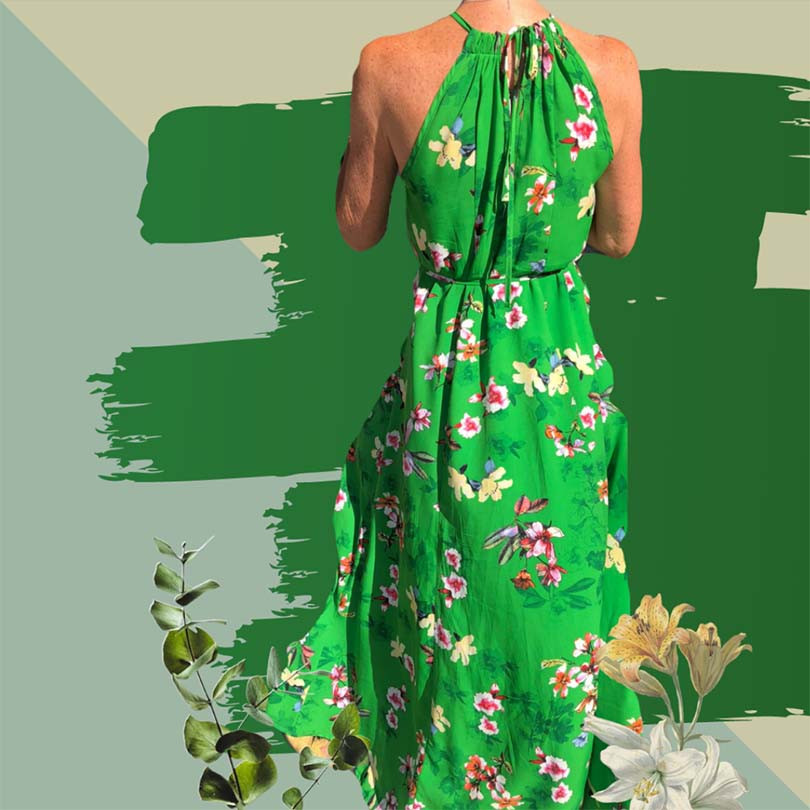 Model wearing green floral print dress, showing back detail in front of wall with wallpaper decorations.